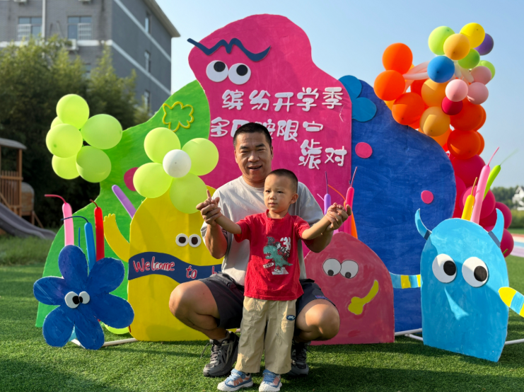 开学现场，大人与孩子在色彩缤纷、布置可爱的背景前合影，氛围欢乐。
       全媒体记者 李水龙文/图